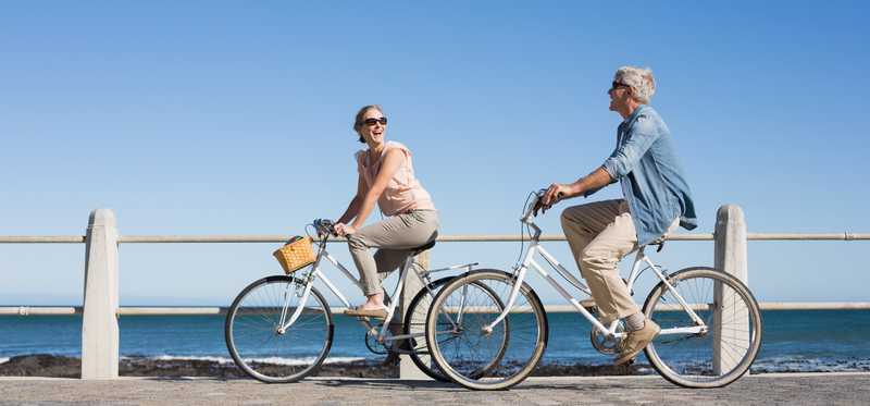 A couple riding bikes on a boardwalk by the beach.