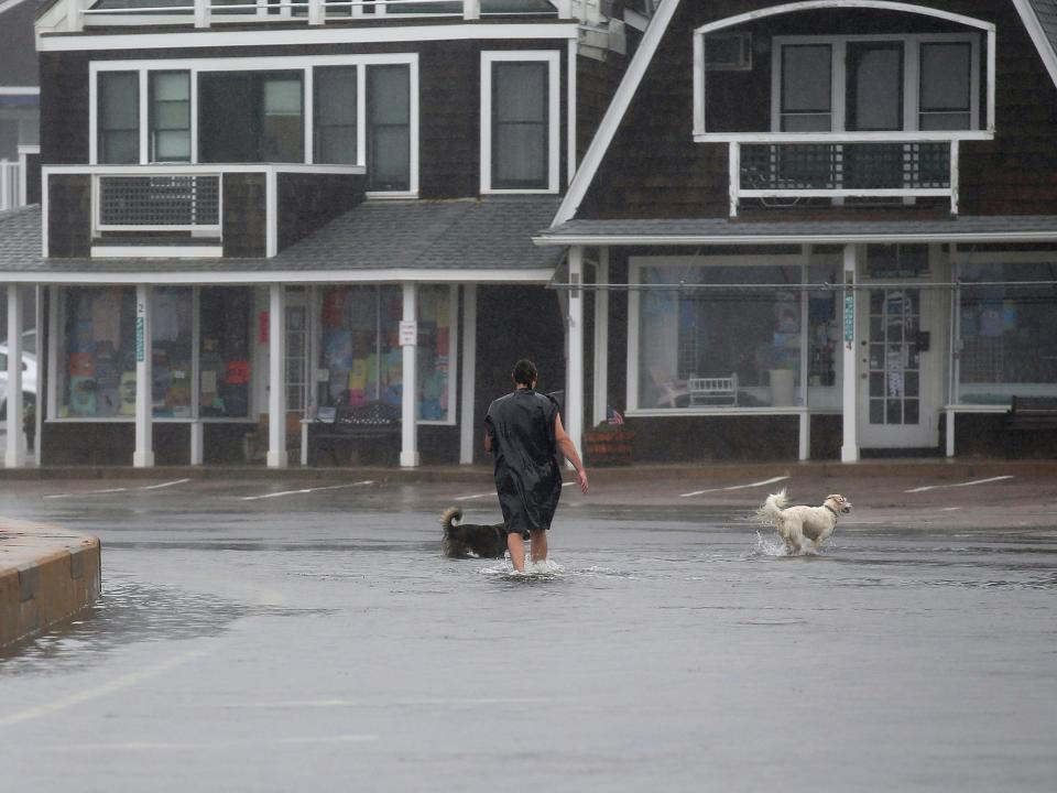 An unidentified man walks his dogs through a flooded parking lot in the Watch Hill section of Westerly, R.I., after Tropical Storm Henri made landfall, Sunday, Aug. 22, 2021.