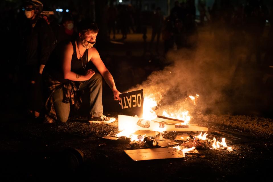 A protester burns signs during a break in confrontations between federal agents and a large crowd at the federal courthouse in Portland, Ore., in the early hours of July 26, 2020.