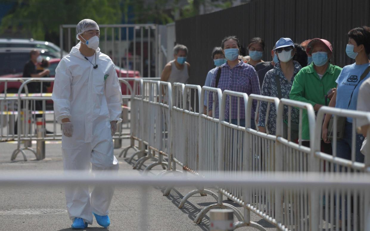 A worker in protective clothing watches over people as they wait in line to undergo COVID-19 coronavirus swab tests at a testing station in Beijing - GREG BAKER/AFP