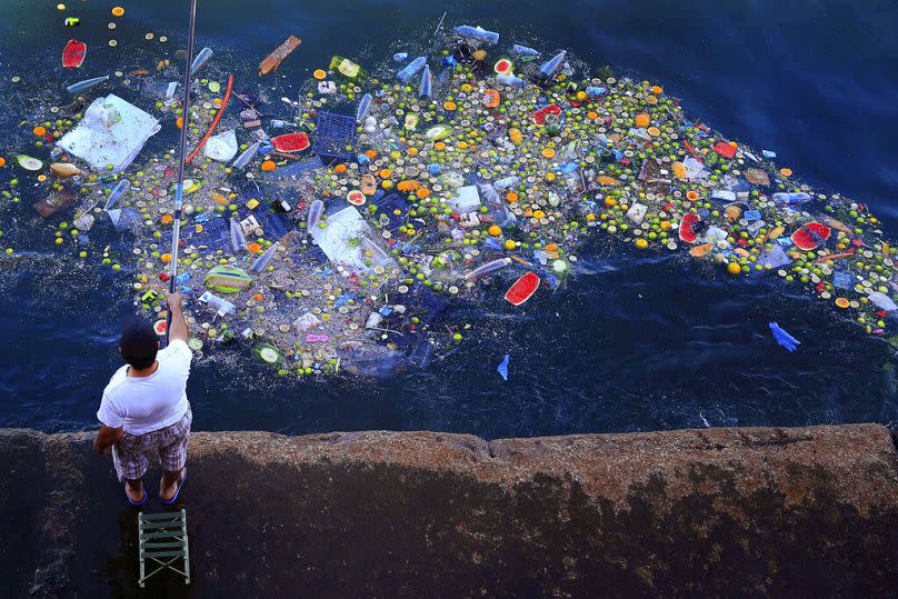 A man holds a fishing rod as floating trash hits the Mediterranean Sea coastline in Beirut, September 2016