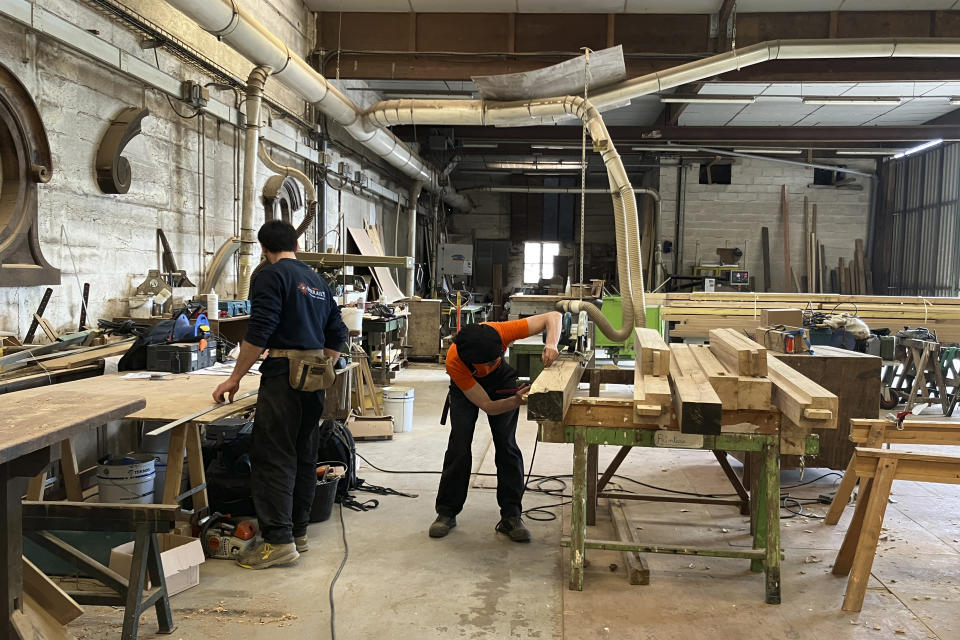 Carpenters work on wooden pieces, part of the new roof for the Notre Dame de Paris cathedral, Thursday, May, 25, 2023, near Angers, western France. Carpenters building a new timber frame for the fire-ravaged roof of Paris' Notre Dame Cathedral are using the same tools and techniques as their medieval predecessors. For them, working with hand-axes to fashion oak beams has been like stepping back in time. (AP Photo/Jeffrey Schaeffer)