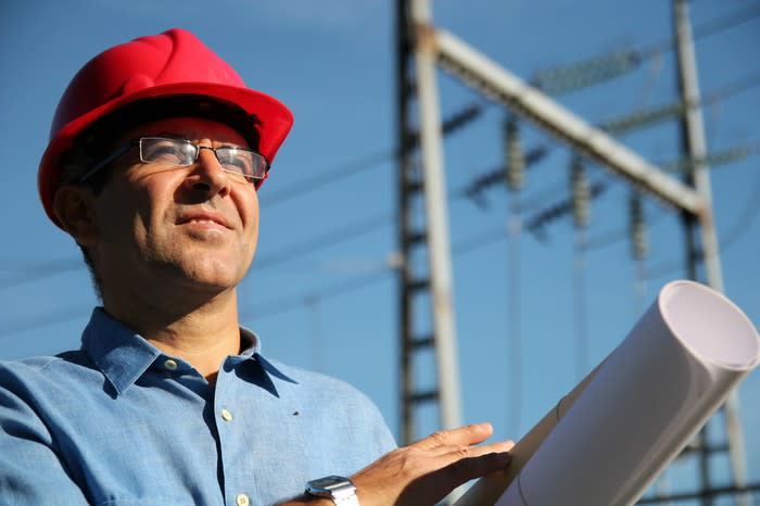 A man with blueprints and high voltage power lines behind him