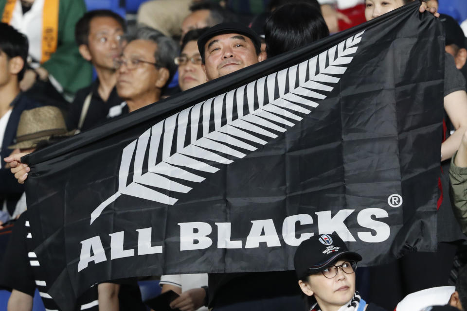 FILE - In this Sept. 21, 2019, file photo, a New Zealand fan holds an All Blacks flag and cheers for his team ahead of the start of the Rugby World Cup Pool B game between New Zealand and South Africa in Yokohama, Japan. New Zealand’s top rugby players have agreed to a 50 percent pay freeze as New Zealand Rugby contends with the financial fallout from the coronavirus outbreak. (AP Photo/Shuji Kajiyama, File)