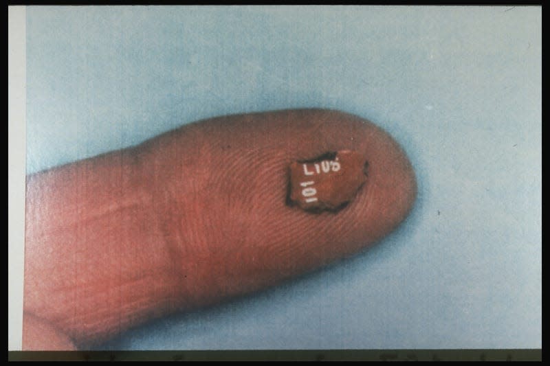 Fingertip-held Toshiba radio fragment recovered fr. 1988 Lockerbie bomb-blasted Pan Am flight 103 plane, Justice Dept. evidence in indictment of 2 Libyans.