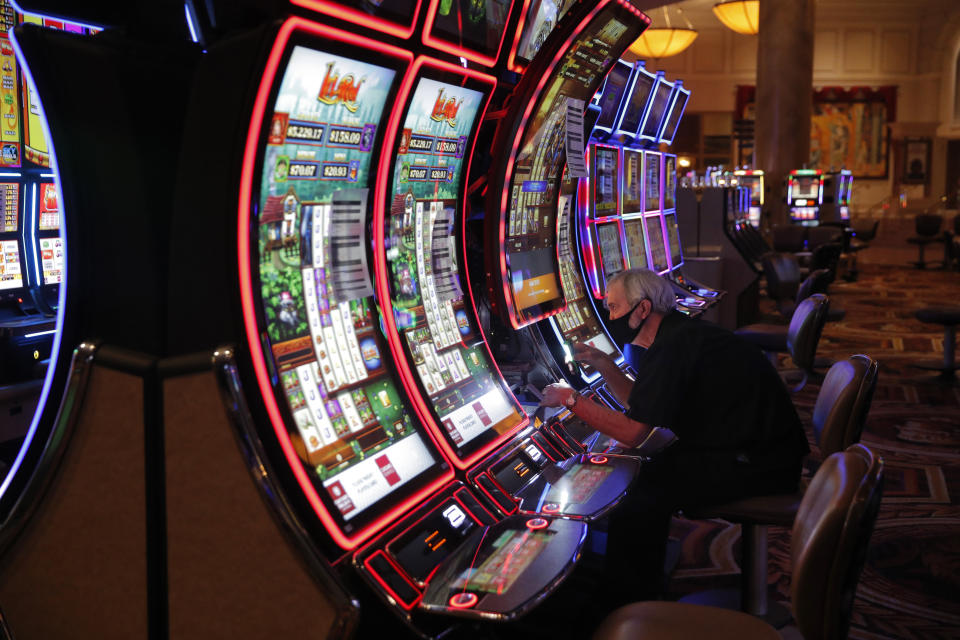 A worker works on an electronic slot machine as chairs have been removed from some machines to maintain social distancing between players at a closed Caesars Palace hotel and casino Thursday, May 21, 2020, in Las Vegas. Casino operators in Las Vegas are awaiting word when they will be able to reopen after a shutdown during the coronavirus outbreak. (AP Photo/John Locher)