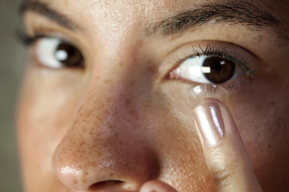 Eye contact from a pretty young mixed race woman inserting a contact lens into her eye.  Macro focus on the lens and eyelash.