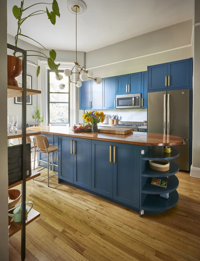 A gray painted kitchen with blue cabinets and stainless steel appliances in a studio apartment.