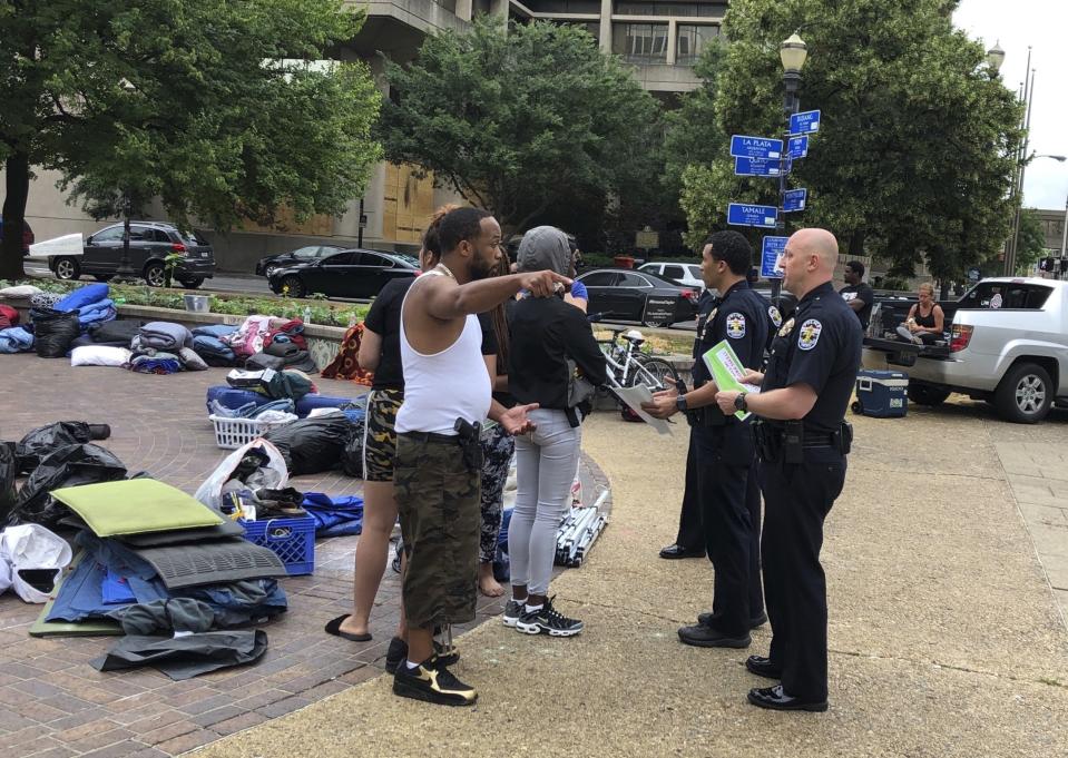 A protester speaks with Louisville police officers who were handing out flyers on an overnight camping ban in Louisville, Ky., on Sunday, June 28, 2020. The park has been the site of protests for weeks after the police killings of Breonna Taylor and George Floyd and police are investigating a deadly shooting that occurred nearby on Saturday night. (AP Photo/Dylan Lovan)