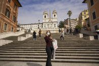 FILE - In this Thursday, March 5, 2020 file photo, a woman wearing a mask poses for photos at the bottom of the Spanish Steps, in Rome. The focal point of the coronavirus emergency in Europe, Italy, is also the region's weakest economy and is taking an almighty hit as foreigners stop visiting its cultural treasures or buying its prized artisanal products, from fashion to food to design. Europe’s third-largest economy has long been among the slowest growing in the region and is the one that is tallying the largest number of virus infections outside Asia. (AP Photo/Andrew Medichini, File )