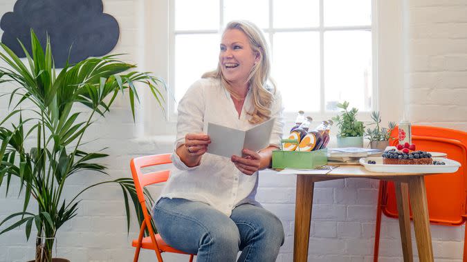 A mid adult woman reads a birthday card she has received from her colleagues, a birthday cake can be seen on the table beside her.