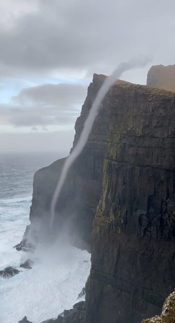 Video grab from the amazing footage of water flowing upwards on the  cliffs off Suðuroy in the Faroe Islands - a phenomenon known as a water spout. See SWNS story SWOCvortex. This is the incredible moment water flowed UPWARDS - after waves were caught in a rare sea vortex. Samy Jacobsen, 41, was out walking along the cliffs off Suðuroy in the Faroe Islands when he spotted a whirlwind of water rising from the waves. He watched as the vortex of spray climbed up the side of the 470m sea cliff - known as Beinisvørð - and billowing on to the cliff top, on Monday. Weather experts said it was a water spout - a spiralling pillar of air - which forms like a tornado over the water when a cliff edge spins the wind in a circle.  