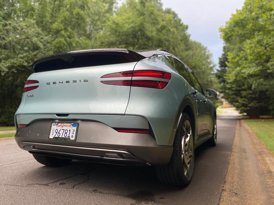 The passenger side rear corner of a green Genesis GV60 Performance EV SUV parked on the side of a street.