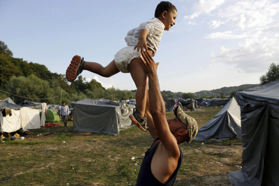 In this photo taken on Monday, Aug. 13, 2018, a migrant man plays with his son in a makeshift migrant camp in Velika Kladusa, 500 kms northwest of Sarajevo, Bosnia. Impoverished Bosnia must race against time to secure proper shelters for at least 4,000 migrants and refugees expected to be stranded in its territory during coming winter. The migrant trail shifted toward Bosnia as other migration routes to Western Europe from the Balkans were closed off over the past year. (AP Photo/Amel Emric)