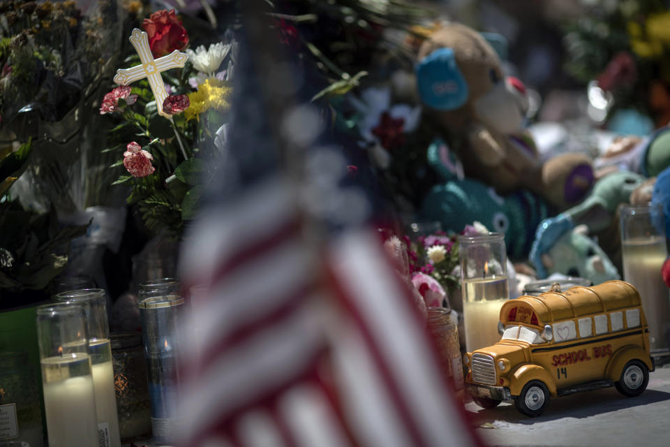 A toy yellow school bus is placed in front of a cross to honor Rojelio Torres, one of the children killed during the mass shooting in Robb Elementary School, while an American flag is seen in the foreground, Sunday, May 29, 2022, in Uvalde, Texas. (AP Photo/Wong Maye-E)