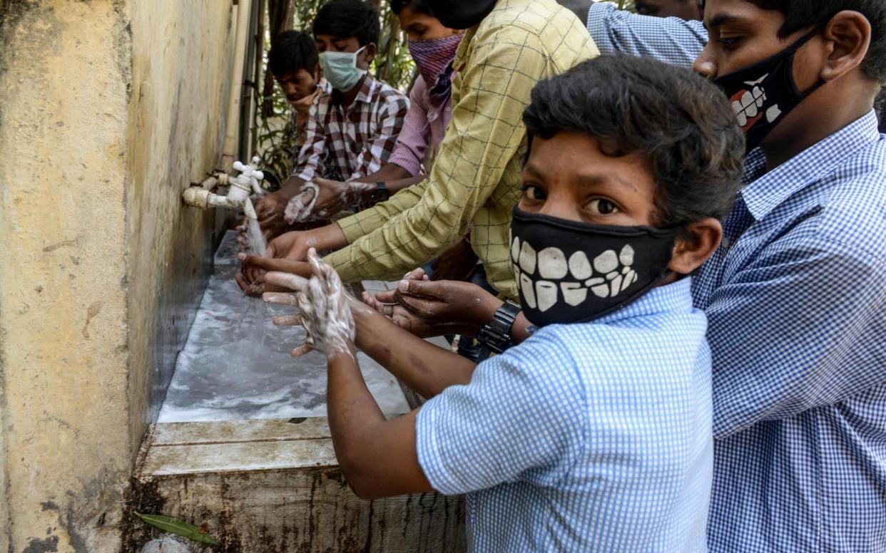 Students wearing facemasks wash their hands before attending a class at a governement-run high school in Secunderabad, the twin city of Hyderabad, India - NOAH SEELAM /  AFP