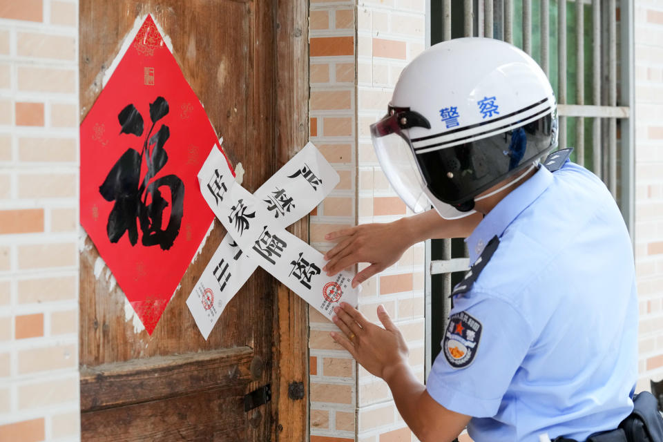 SANYA, CHINA - AUGUST 17: A policeman sticks a seal reading 'home isolation' to a door at a locked down community on August 17, 2022 in Sanya, Hainan Province of China. The community was locked down after being designated as a high-risk area for COVID-19. (Photo by Wu Wei/VCG via Getty Images)