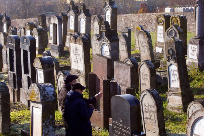 Two men stand in front of graves desecrated with swastikas at the Jewish cemetery in Westhoffen