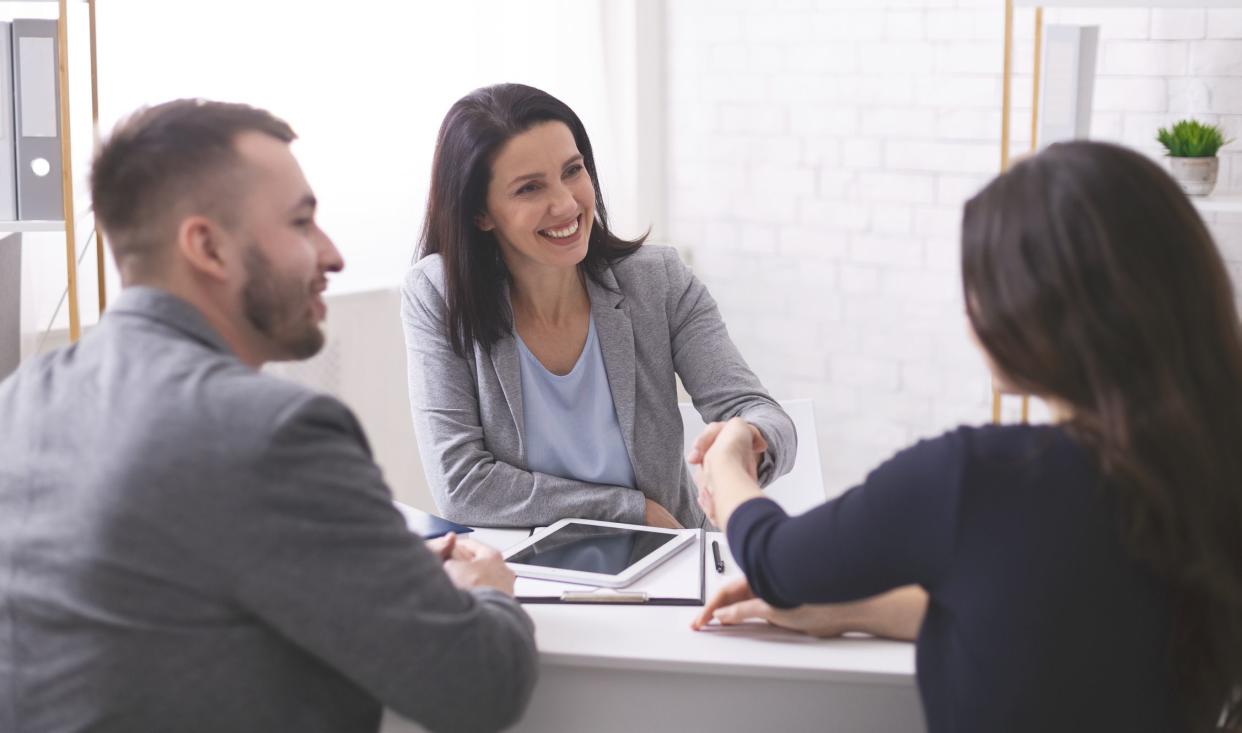 Deal. Positive insurance broker handshaking with young couple after signing agreement contract