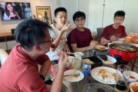 Malaysian students, from left, Felix Mong, Jason Ong, Ter Leong Kern and Siew Ee Sung eat bak kwa, a Chinese meat product similar to jerky, during a Lunar New Year hot pot lunch hosted by a Malaysian couple at their rented apartment in Singapore, Saturday, Feb. 13, 2021. With Malaysian workers and students stranded in the city state over the Lunar New Year due to coronavirus travel restrictions, the Malaysian Association in Singapore has called on Malaysians to treat students to a meal. (AP Photo/Annabelle Liang)