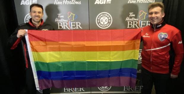 John Epping, left, and Greg Smith hold up a Pride flag following their match in the Brier in Calgary on March 9. (Greg Smith/Twitter - image credit)