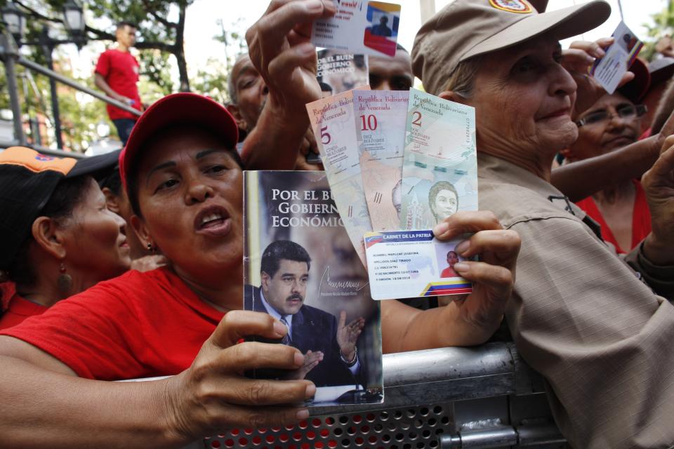 FILE - In this Aug. 21, 2018 file photo, pro-government supporters cheer as some hold up new banknotes and patriot identification cards during a rally in Caracas, Venezuela. Little noticed abroad amid the turmoil unleashed by the opposition’s renewed push to oust President Nicolas Maduro in early 2019, Venezuela’s central bank devalued the country’s bolivar currency on Jan. 28, 2019 by 50 percent, eclipsing the parallel black market rate. (AP Photo/Ariana Cubillos, File)