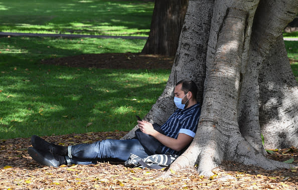 A man wearing a face mask reads his mobile phone as people gather in the Domain in Sydney, Australia. 