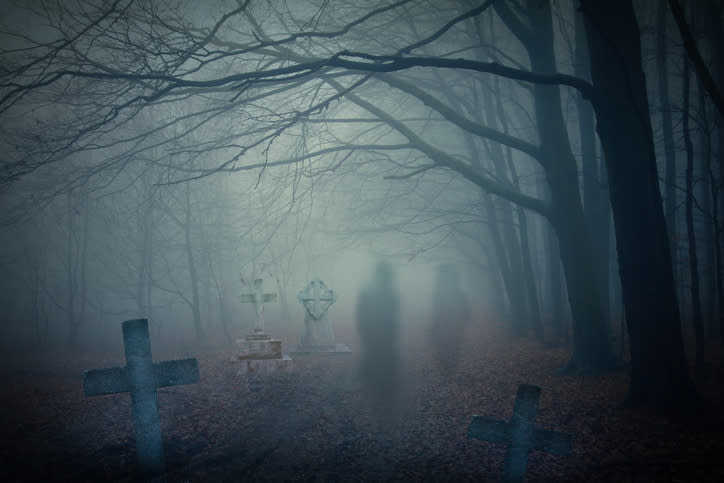 Foggy graveyard scene with shadowy, ghost-like figures among gravestones and bare trees