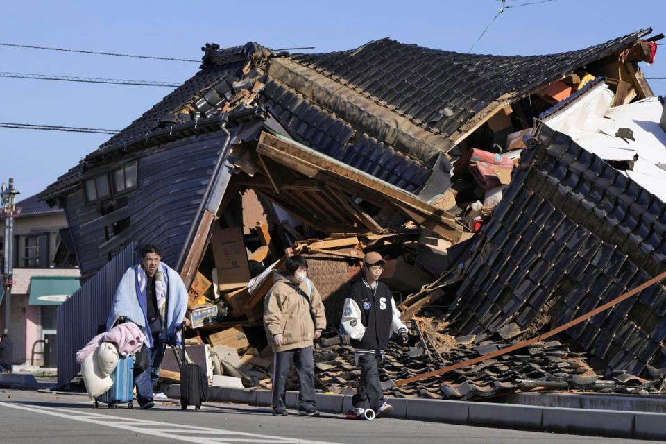 A man carries his belongings past a collapsed house following an earthquake in Wajima, Ishikawa prefecture (AP)