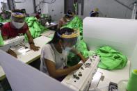 Workers wearing face mask and face shield to help curb the spread of the new coronavirus, sew behind white partition surrounding their sewing tables as they work at a garment factory Thursday, May 28, 2020, at Industrial Zone in Yangon, Myanmar. Despite a poor public health infrastructure and crowded urban areas, Myanmar has reported a surprising low number of COVID-19 cases, with just a little over 200 confirmed and a few deaths. (AP Photo/Thein Zaw)