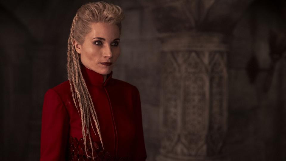 Liandrin, wearing red with her hair in braids, stands in a corridor in The Wheel of Time