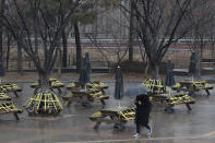 A man wearing a face mask as a precaution against the coronavirus walks past benches and tables taped for social distancing in Seoul, South Korea, Thursday, Jan. 21, 2021. (AP Photo/Lee Jin-man)