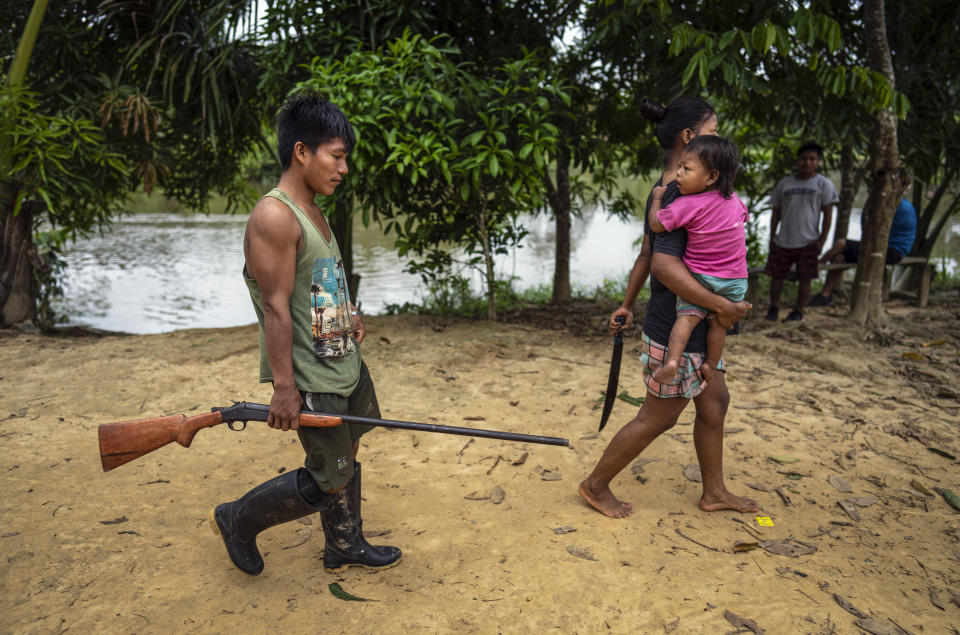 Maijuna youth Cliver Padilla walks with his wife and daughter to the outskirts of the town to hunt animals for the day's meals, in Sucusari, Peru, Thursday, May 30, 2024. In the community of thatched houses, the routine of the some 180 inhabitants is mostly traditional. They fish, hunt and grow fruit for local markets, mostly aguaje, an Amazon delicacy. (AP Photo/Rodrigo Abd)