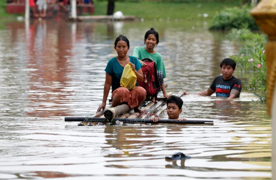 Flood victims wade through floodwaters on a makeshift raft during flooding in Taungo (EPA)