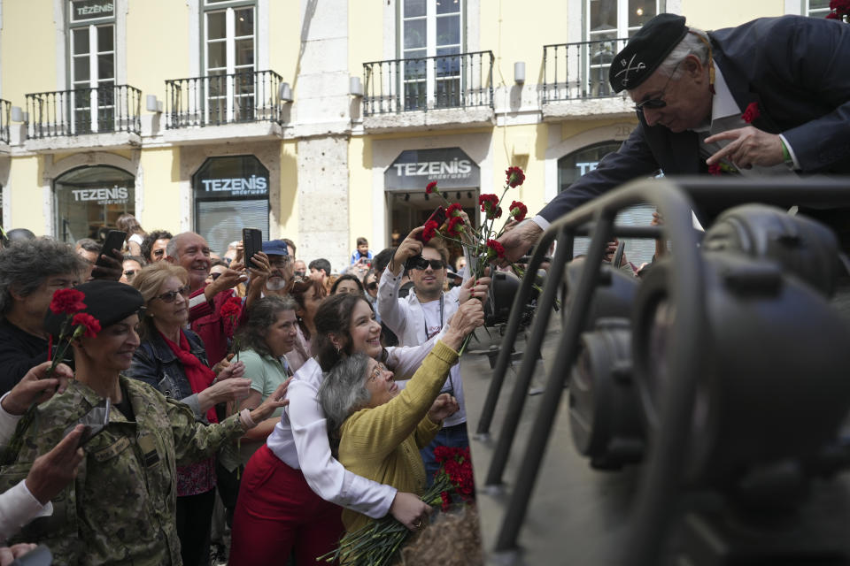 Celeste Caeiro, 90, hands red carnations to former army captain Manuel Correia Silva, in Lisbon, Thursday, April 25, 2024, during the reenactment of troops movements of fifty years ago, part of anniversary celebrations of the Carnation Revolution. (AP Photo/Ana Brigida)