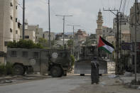 Palestinian activist Khairi Hanoon waves the Palestinian flag as a convoy of Israeli military armored vehicles drives by during an army raid in Tulkarem, West Bank, on Tuesday, Sept. 3, 2024. (AP Photo/Majdi Mohammed)