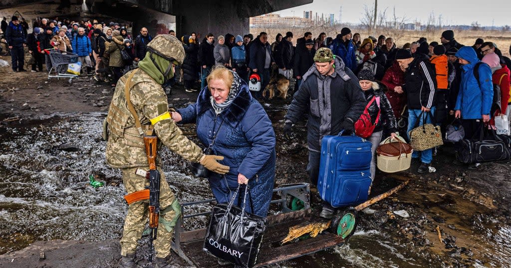 This picture taken on March 7 shows a Ukrainian serviceman helping evacuees gathered under a destroyed bridge as they flee the town of Irpin  (AFP via Getty Images)