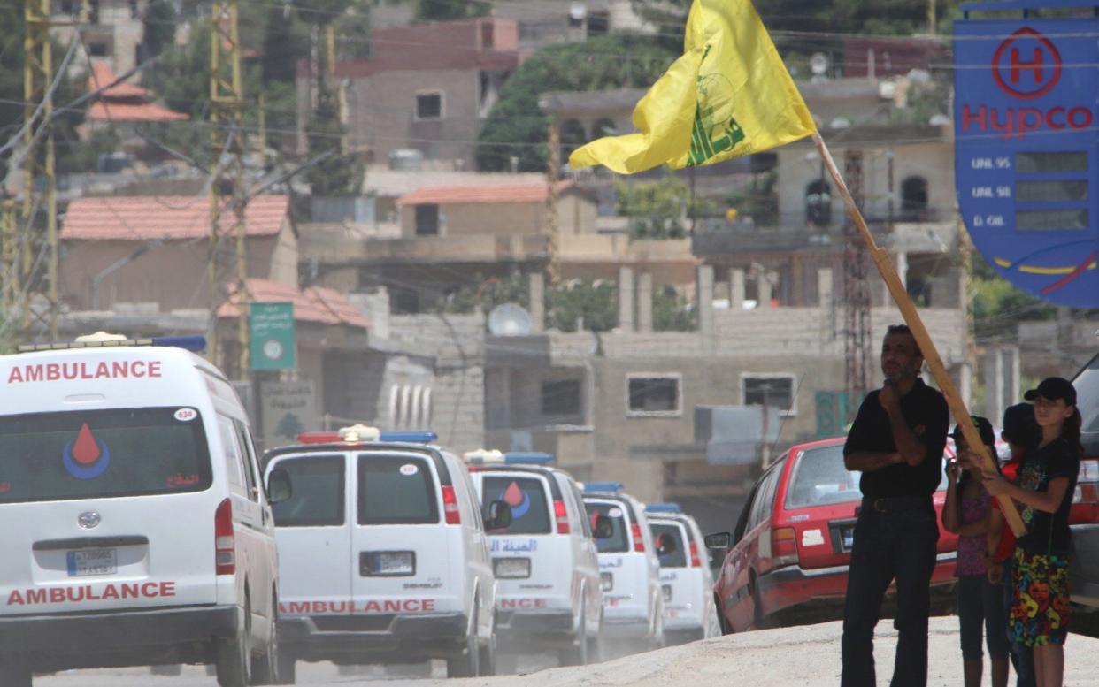 People wave a flag of the Lebanese Shiite Hezbollah movement as the group's ambulance convoy drives past carrying bodies of fighters  - AFP