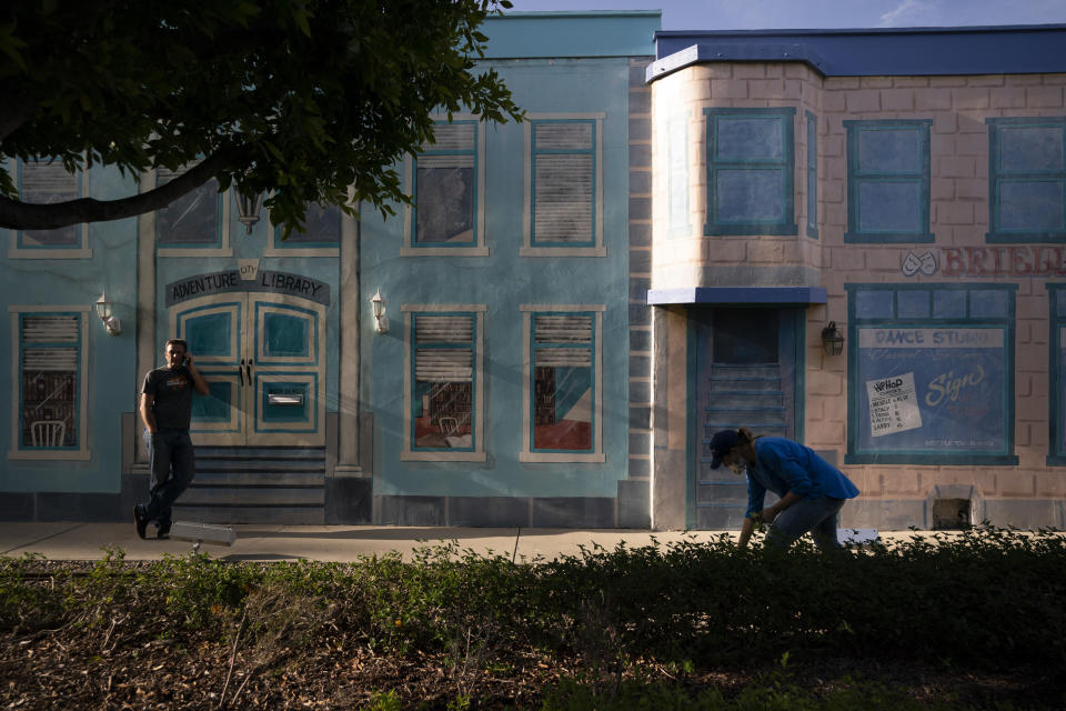 Allan Ansdell Jr., left, owner and president of Adventure City amusement park, talks on the phone as his wife, Trina, who is in charge of the park's human resources, pulls weeds ahead of its reopening in Anaheim, Calif., Wednesday, April 14, 2021. The family-run amusement park that had been shut since March 2020 because of the coronavirus pandemic reopened on April 16. (AP Photo/Jae C. Hong)