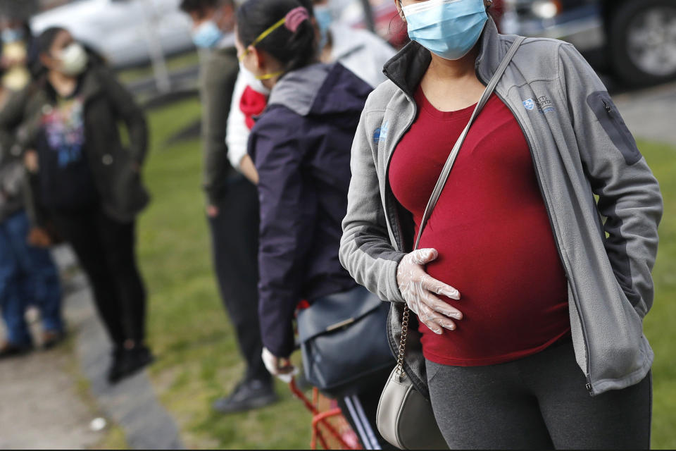 A pregnant woman holds her belly as she waits in line for groceries with hundreds during a food pantry sponsored for those in need due to the COVID-19 pandemic in Waltham, Mass., on May 7, 2020. (AP Photo/Charles Krupa) 