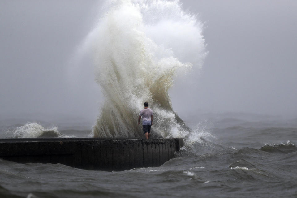 A wave crashes as a man stands on a jetty near Orleans Harbor in Lake Pontchartrain in New Orleans, Sunday, June 7, 2020, as Tropical Storm Cristobal approaches the Louisiana Coast. (AP Photo/Gerald Herbert)