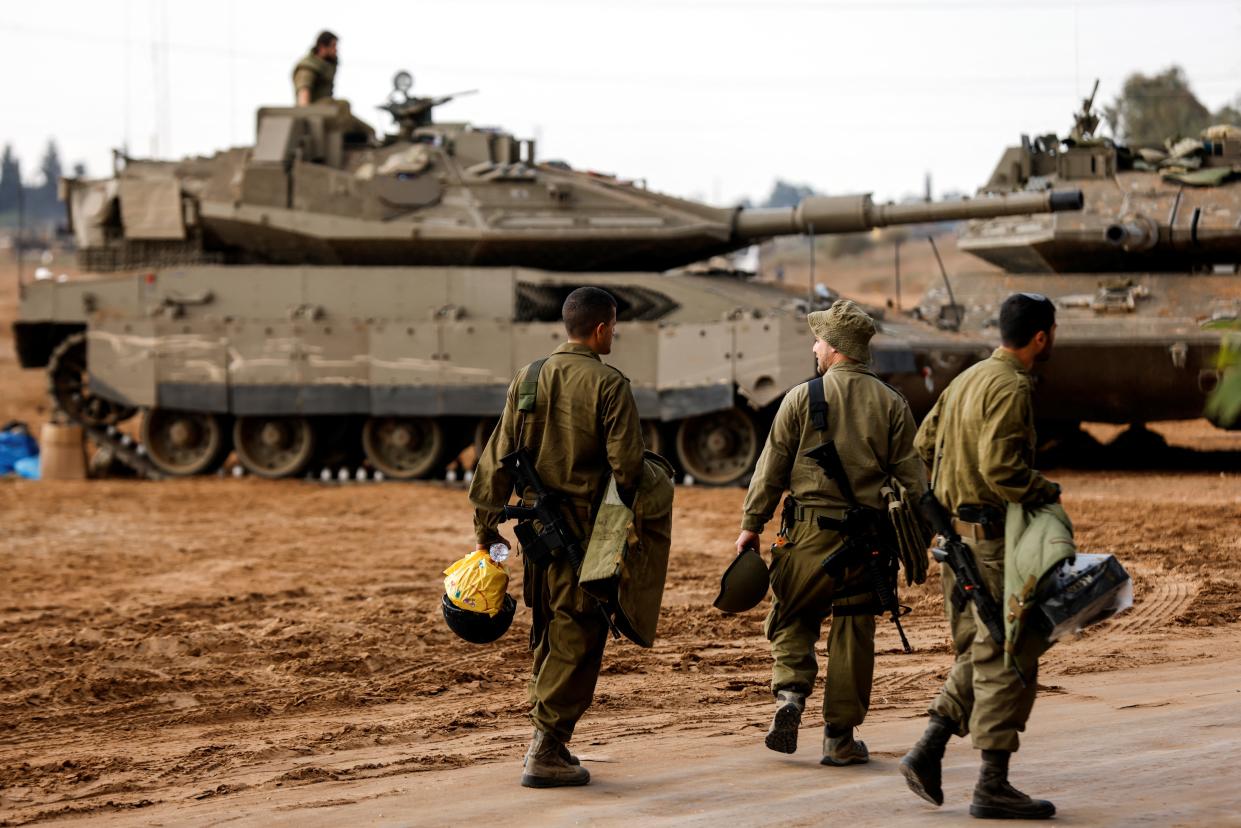 Three Israeli soldiers walk past tanks near Israel’s border with Gaza (REUTERS)