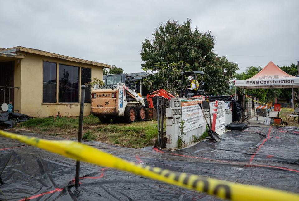 Heavy machinery, tarps and tents occupy the lawn of a residential home.