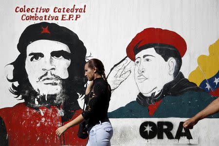 A woman walks past a mural depicting Venezuela's late President Hugo Chavez (R) and Cuban revolutionary hero Ernesto "Che" Guevara, near the National Assembly building in Caracas December 23, 2015. REUTERS/Carlos Garcia Rawlins