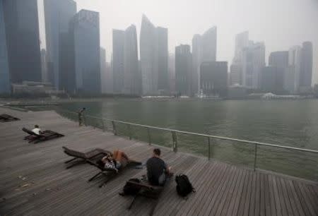 People sit on deck chairs near the city skyline shrouded by haze in Singapore October 23, 2015. REUTERS/Edgar Su