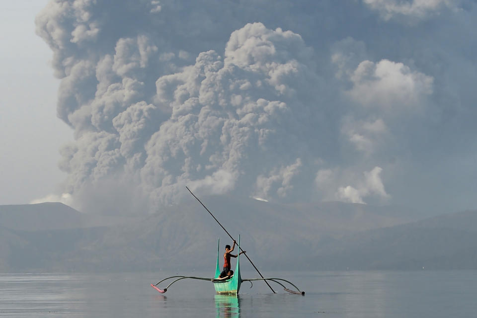 TOPSHOT - A youth living at the foot of Taal volcano rides an outrigger canoe while the volcano spews ash as seen from Tanauan town in Batangas province, south of Manila, on January 13, 2020. - The Philippines was on alert January 13 for the "explosive eruption" of a volcano south of Manila, which officials said could be imminent after a massive column of ash forced a halt to flights at the capital's main airport. (Photo by Ted ALJIBE / AFP) (Photo by TED ALJIBE/AFP via Getty Images)