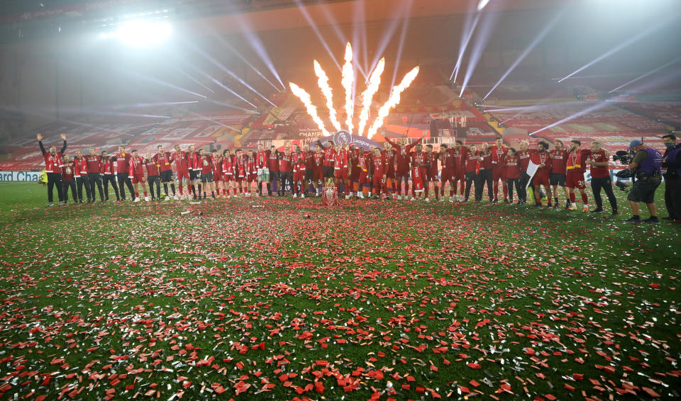 Liverpool players celebrate with the Premier League trophy at an empty Anfield stadium.