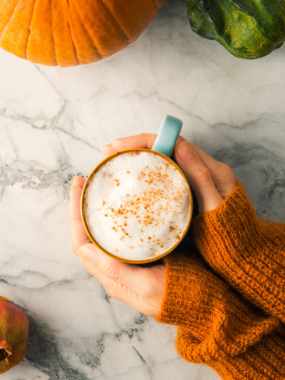 A woman holding a latte in a mug on marble table.