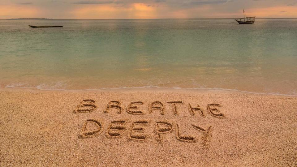 A beach at sunset where there is an inscription on the sand "Breathe deeply".