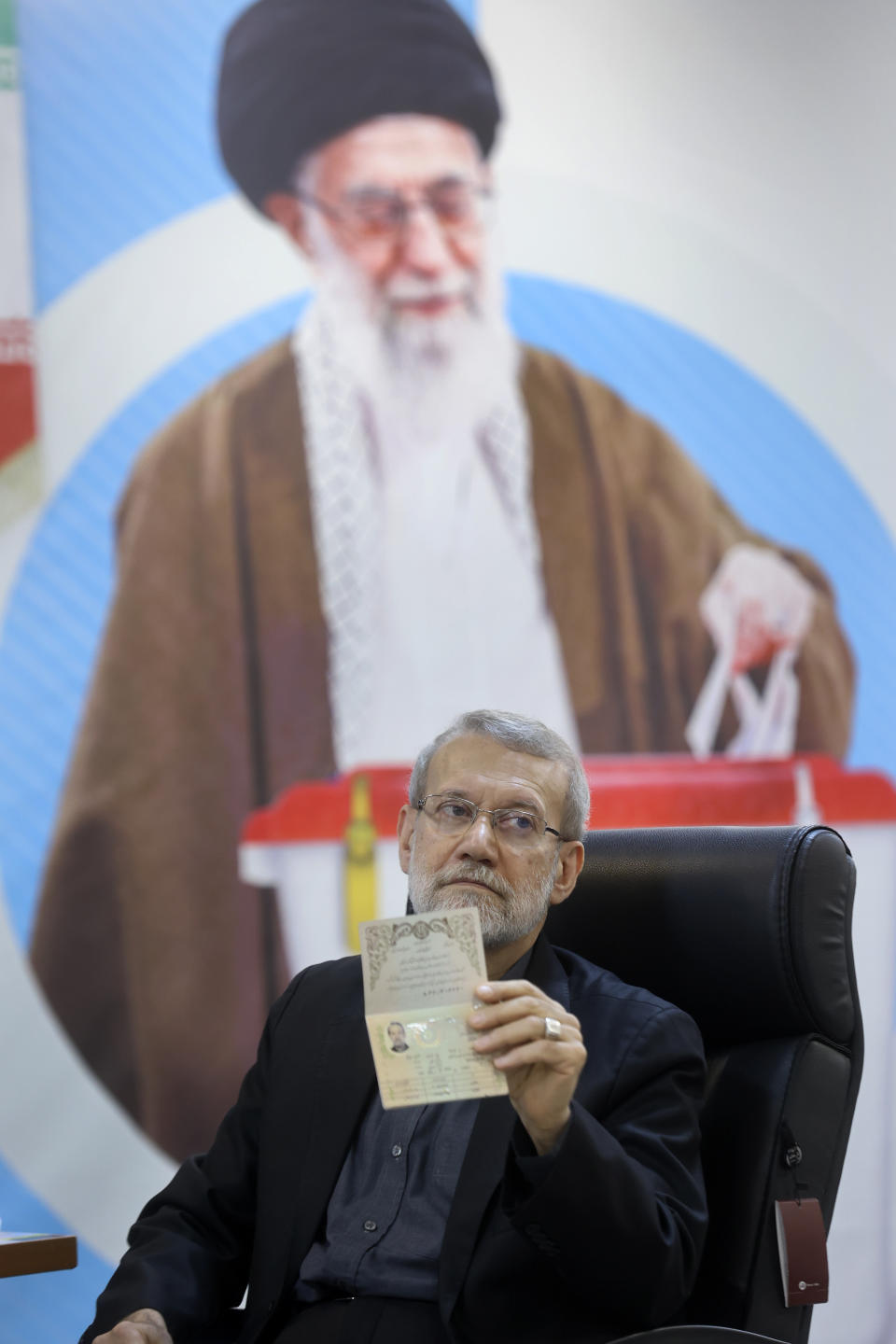 Former Iran's parliament speaker Ali Larijani shows his identification document to media beside a portrait of the Supreme Leader Ayatollah Ali Khamenei while registering his name as a candidate for the June 28 presidential elections at the Interior Ministry in Tehran, Iran, Friday, May 31, 2024. Larijani registered Friday as a possible candidate in the Islamic Republic's presidential election to replace the late Ebrahim Raisi, who was killed in a helicopter crash earlier this month with seven others. (AP Photo)